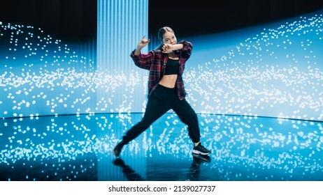 Stylish Young Professional Female Dancer Performing A Hip Hop Dance Routine In Front Of Big Led Wall Screen With VFX Animation During A Virtual Production In Studio Environment. 105 BPM Song.