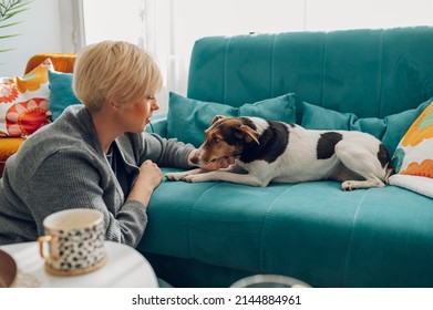 Stylish Young Woman Bonding And Spending Time With Her Dog Pet On The Couch In The Living Room. Adorable Friendship Between Animal And Human. National Dog Day.