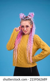 Stylish Young Woman With Colorful Hair And Afro Braids, Dreadlocks Looking In Camera, Touching Sunglasses. Confident Creative Person Studio Portrait, With Blue Background