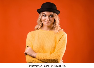 Stylish Young Woman In Knitted Clothes And Bowler Hat, Bright Orange Background, Studio Portrait