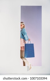 Stylish Young Woman With Shopping Bag Stepping Through Aperture On Grey