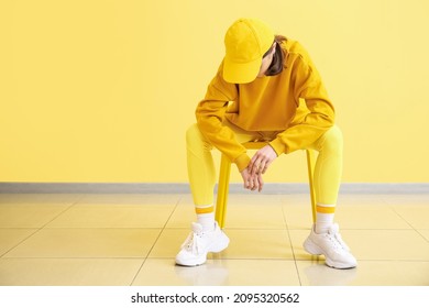 Stylish Young Woman Sitting On Chair Near Yellow Wall