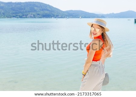 stylish young woman smiles. lake and mountains. girl in sunglasses and boater
