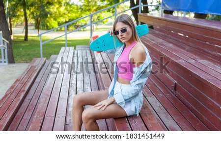 Stylish young woman in sunglasses dressed in summer youth clothing holds a cruiser board outdoors