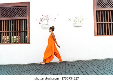 Stylish Young Woman Walking In The City In Orange Dress Against White Wall. Chic Traveller Tourist On A City Tour. Street Style, Copy Space.