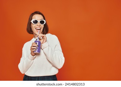 Stylish young woman in white trendy sunglasses sipping soda drink from can on orange backdrop - Powered by Shutterstock