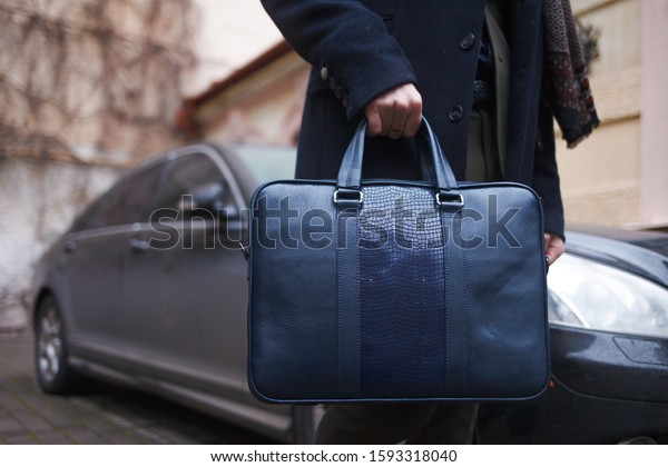 Stylishly dressed business man\
with a bag in his hands stands on the background of his\
car\
