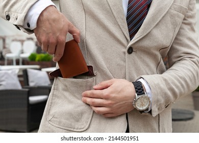 A Stylishly Dressed Business Man Puts A Brown Leather Wallet In His Jacket Pocket. Horizontal Orientation, No Face 