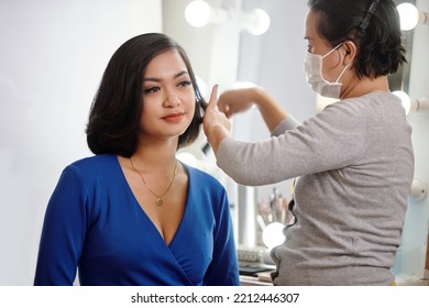 Stylist In Mask Cutting Hair And Making Hairstyle To Young Model In Beauty Salon