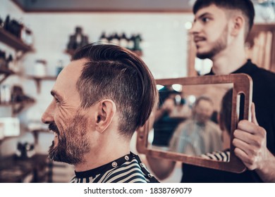 The stylist shows the client a mirror to examine the hairstyle from behind. A man sits in a barbershop chair and smiles after finishing a haircut. - Powered by Shutterstock