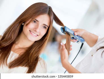 Stylist Using A Hair Straightener On A Woman At The Salon