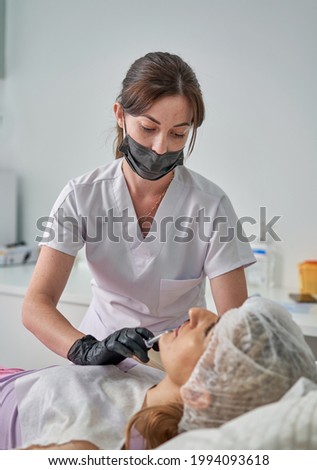 Stylist's hands in black gloves wipe the model face with a cotton pad. Beautiful attractive female face of a blonde well-groomed woman or lady. Styling and lamination of eyebrows.