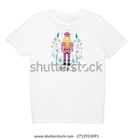 A stylized nutcracker figure in pink and blue uniform stands within a colorful floral border on a white t-shirt.