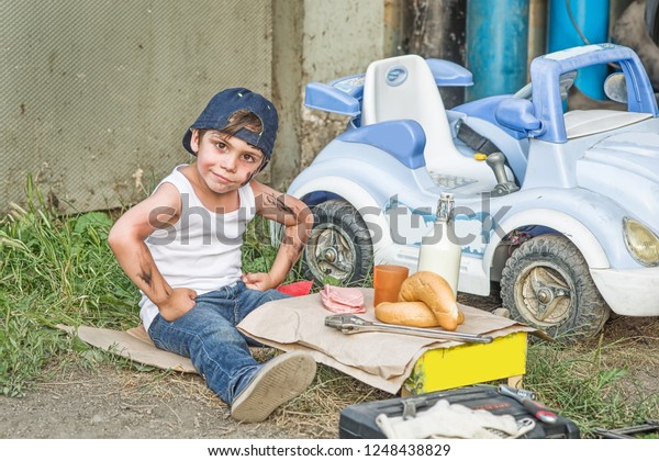 Stylized portrait of a boy in a tank,\
jeans and a baseball cap in the garage repairing the\
car.