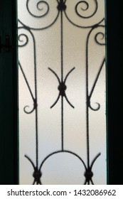 Stylized Wrought Iron Window Bars Through Frosted Textured Glass Seen From The Inside Looking Out.