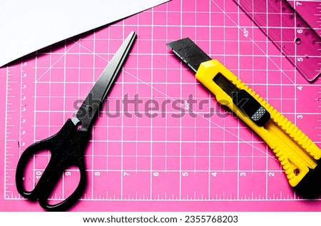 Stylus, ruler and scissors on a pink cutting board in top view angle