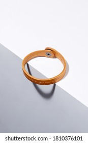 Subject Shot Of Ginger Bracelet Made As Leather Strap With Middle Stitch And Steel Snap Fastener. The Simple Stylish Bracelet Is Located On The Edge Of White Surface.