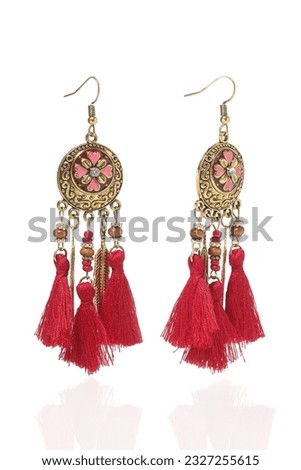 Subject shot of golden long graceful boho style earrings decorated with colored enamel, beads and red tassels made of cotton threads. The earrings are isolated on the white background.