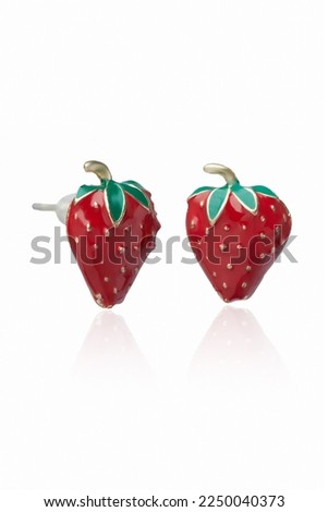 Subject shot of golden stud earrings made as strawberries decorated with bright colored enamel. The original earrings are isolated on the white background. Vogue accessory for ladies and girls.