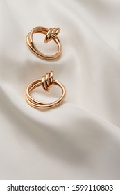 Subject Shot Of A Pair Of Golden Earrings Isolated On The White Textile Surface. Each Earring Is Made As A Set Of Three Glossy Rings And A Large Double Hoop.