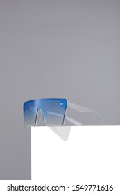 Subject shot square oversized sunglasses and thick white frame   blue lenses  The sunglasses are isolated the white square the gray background  