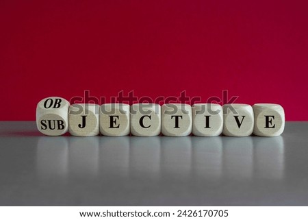 Subjective and objective symbol. Turned a cube and changes the word subjective to objective. Beautiful red background, grey table, copy space. Business, balance or disbalance concept.