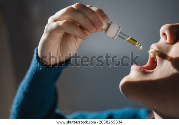 Sublingual cbd hemp oil - Woman taking\
cannabidiol under tongue for anxiety alternative treatment - Focus\
on hand holding\
dropper