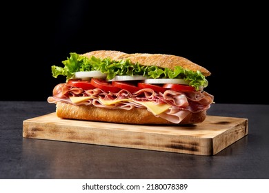Submarine sandwich with ham, cheese, lettuce, tomatoes,onion, mortadella and sausage on wooden table - Shutterstock ID 2180078389