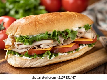 Submarine Sandwich Made With Turkey, Ham, Cheese Lettuce And Tomato On A Hoagie Roll With Lettuce And Tomatoes In Background