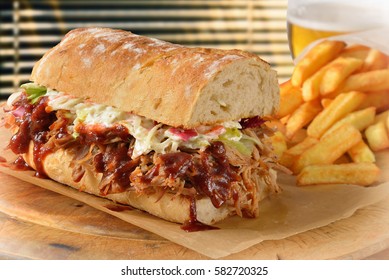Submarine sandwich with pulled pork, BBQ sauce, coleslaw salad dressing, a serving of fries and a glass of beer. 