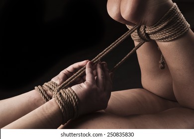 Submissive woman in hog tie bondage position on black background / BDSM theme