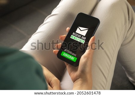 Subscribe newsletter concept on a mobile phone or smartphone. Woman indoors holding mobile phone with newsletter join, sign up and register page