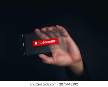 Subscription concept. Big red subscribe button with bell icon on the screen of futuristic transparent glass phone technology in hand. Super slim transparent future smartphone on dark background.