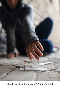 Substance Abuse, Addiction, People And Drug Use Concept - Close Up Of Addict Woman Reaching To Used Syringes On Ground