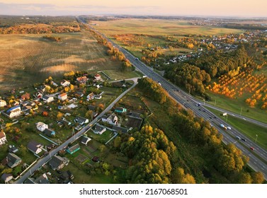 Suburb houses in rural, aerial view. Car and truck driving on road. Roofs of suburban houses in countryside. Houses and rural buildings in fall colors on sunset. Highway traffic with car and trucks.