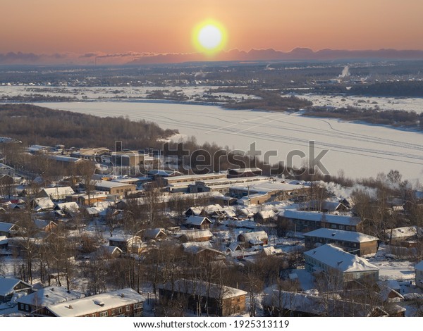 A suburb, village, or industrial quarter of a\
winter city (panorama from skyscraper). Russian hinterland, view of\
the frozen ice of the Vyatka River. Sunrise, cold dawn over the\
wooden houses.