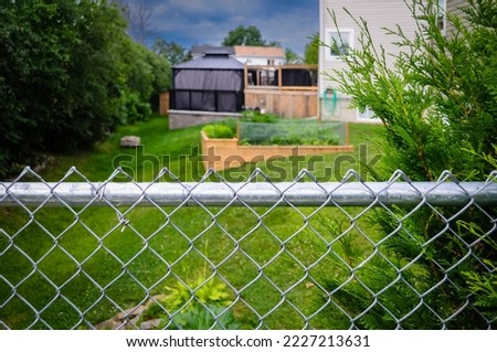 Suburban backyard decks, gazebo and garden behind a chain-link fence on a sunny morning