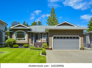 Suburban family house with concrete driveway, wide garage door on blue sky background.