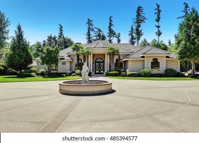 Suburban Family House With Fountain Statue In The Front Yard, Asphalt Driveway. Luxury Residential House With Large Windows, Trees Around And Blue Sky Background. Northwest, USA