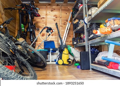 Suburban home wooden storage utility unit shed with miscellaneous stuff on shelves, bikes, exercise machine, ladder, garden tools and equipment. Messy and chaos at house yard barn. Organization order