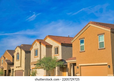 Suburban Homes In Tucson, Arizona With Attached Garage. Row Of Houses With Painted Stucco Walls And Clay Tile Roofs Against The Blue Sky At The Back.