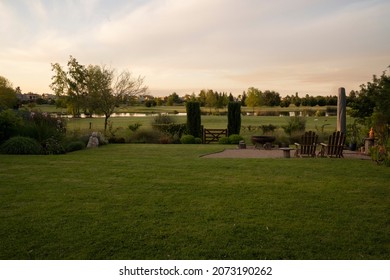 The Suburban House Backyard At Sunset. View Of The Green Grass And Lake In The Background With Beautiful Dusk Colors. 