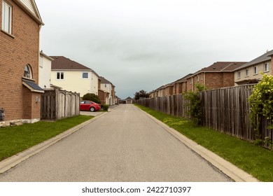 Suburban street lined with well-maintained homes - wooden fences bordering properties - red car parked - overcast sky - greenery peeking through fences. Taken in Toronto, Canada. - Powered by Shutterstock