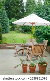 Suburban UK Back Garden In Summer With Patio, Wooden Garden Furniture And A Parasol Or Sun Umbrella