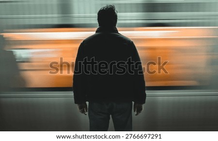 Subway train speeding past an underground metro platform and a back vi̇ew person visible in the foreground.