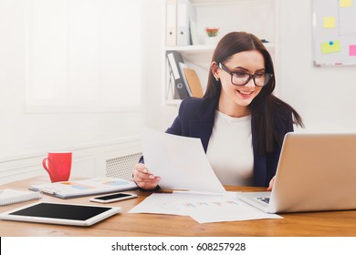 Succesfull Woman, Female Carreer Concept. Beautiful Young Businesswoman Sitting By Wooden Desk With Laptop. Modern Office Worker In White Room Interior.