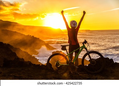 Success, achievement, accomplishment and winning concept with cyclist mountain biking. Winning happy MTB woman cycling reaching goal raising arms at sunset cheering and celebrating at summit top.