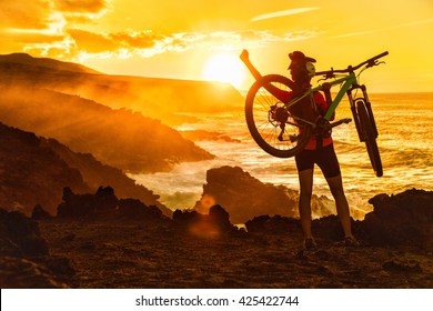 Success, achievement, accomplishment and winning concept with cyclist mountain biking. Happy MTB woman cycling raising arms lifting bike by sea during sunset cheering and celebrating at summit top. - Shutterstock ID 425422744
