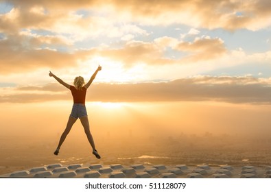 Success concept. Celebrating woman on top of skyscraper overlooking the city at sunrise. 