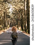 Success and feedom concept with woman and backpack viewed from back and long asphalt road staight in the middle of a high trees nature forest - life after coronavirus lockdown